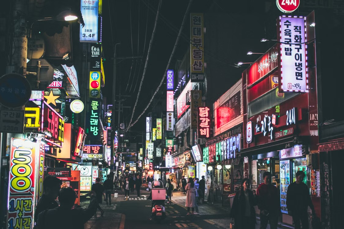 Neon signs lining a busy Seoul side street at night