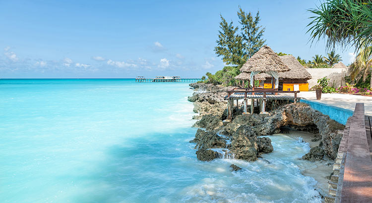 Thatched beach hut on the rocks above turquoise water in Zanzibar